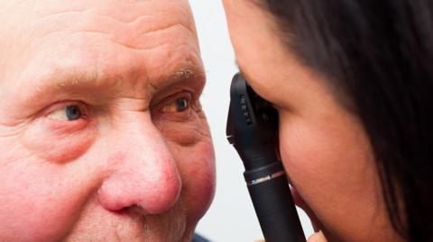 A close up image of an ophthalmologist looking into an elderly man's right eye