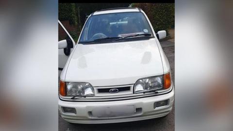 White vintage Ford Cosworth with the front driver door open.