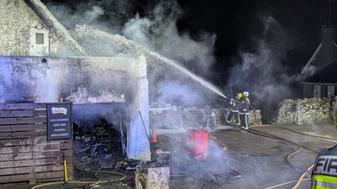 A picture from the scene of the blaze at the pub in Lustleigh. There is a firefighter with a hose aimed at the thatched roof.