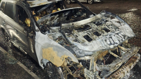 Shows a burnt-out car 