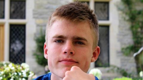 A close-up of Christian Hobbs' face, with his chin resting on is fist. He had short cropped hair and is looking at the camera