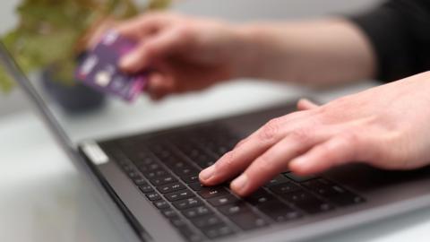 A woman using a laptop as she holds a bank card.
