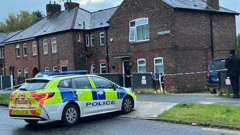 A police car parked in front of a house with police tape around it