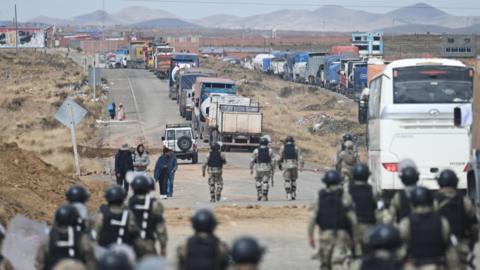 Riot police walk along a road lined with trucks held up by a roadblock in Bolivia
