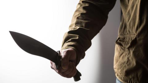 Man holding a large knife in a threatening fashion