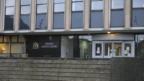 Exterior of the grey, concrete court building. A sign next to the glass doors reads Teesside Justice Centre.