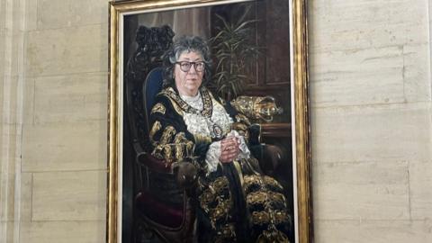 A portrait of councillor Jacqui Rayment, on the wall with a gold frame around it.