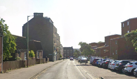 A residential street with houses on each side and cars parked in the street