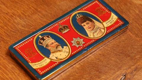 A small tin made by chocolatiers Rowntree shows the King Edward VII and Queen Alexandra in 1902. It has a red case and is made of solid silver.