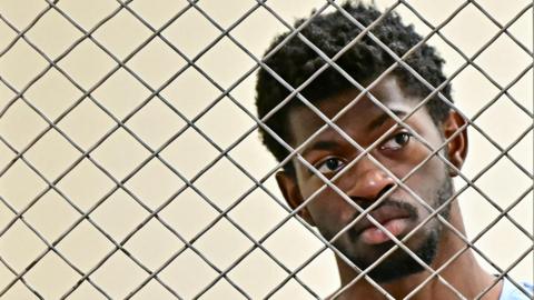 Lil Nas X is behind wire with a blank expression