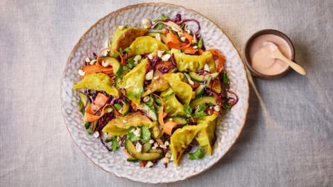 Dumpling salad on a round plate with a small dish of sauce on the side