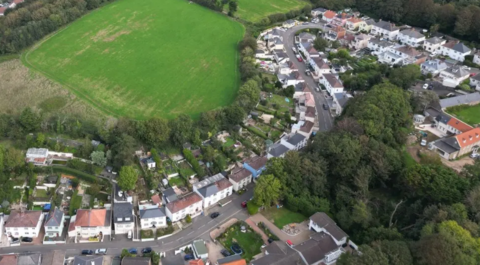 An aerial view of houses in Jersey on an S shaped road, surrounded by fields and trees.
