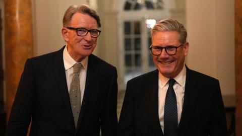 Starmer and Mandelson stood next to each other in suits, smiling.
