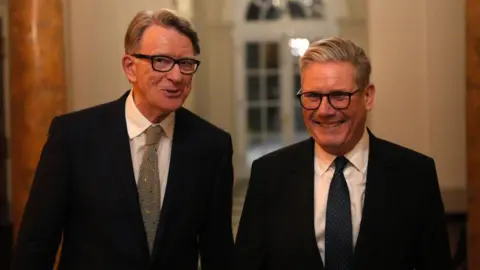 Starmer and Mandelson stood next to each other in suits, smiling.