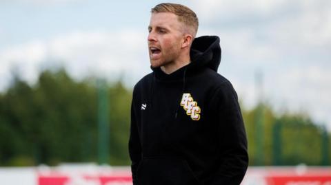 Joe Morrell standing on a training pitch looking towards the left with his hands in his pockets and his mouth open
