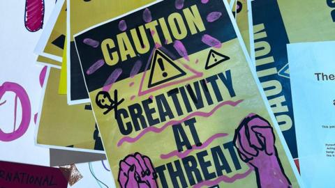 A yellow and purple poster with the words: Caution: Creativity at Threat