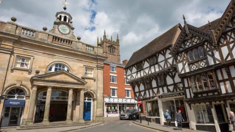 Ludlow town centre with shops in historic buildings, a church tower in the background and a black and white building to the right.