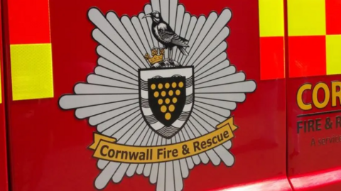 The side of a Cornwall Fire and Rescue Service engine. It is red and has a badge on the side. 