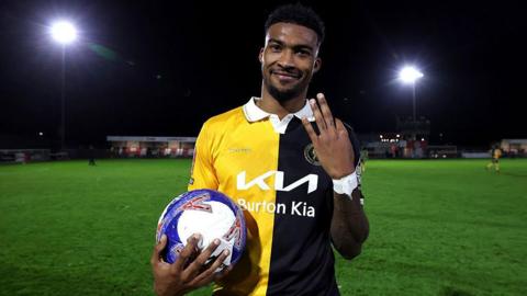 Burton's Tyrese Shade holds up three fingers while holding the match ball