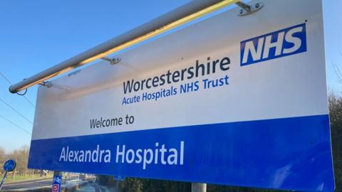 A large blue and white sign saying "Welcome to Alexandra Hospital" with the logo for Worcestershire Acute Hospitals NHS Trust in the top right corner.