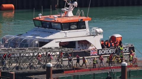 A group of people wearing life jackets being brought off a Border Force vessel at Dover 