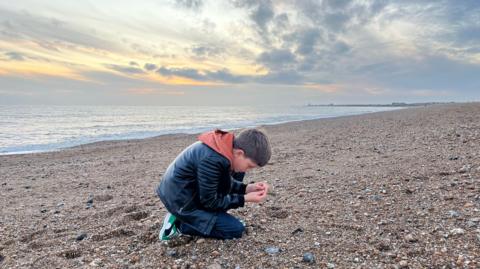 Ben kneeling on a shingle beach in Shoreham where found a Neanderthal hand axe 