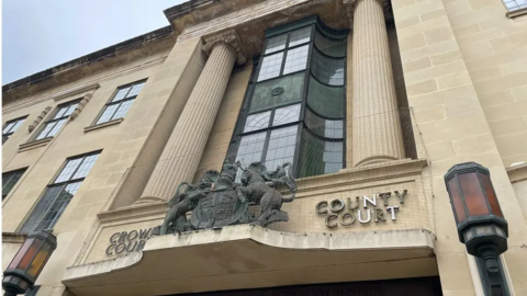 A general view picture of Oxford Crown Court, which is a three-storey building and is made of sand-coloured stone. Crown court and county court are written either side of a court of arms above the main doors in and out of the courthouse 