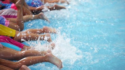 A line of children's legs and feet splashing in a pool.