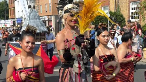 Four people in ornate dresses and headgear march as part of the carnival procession.