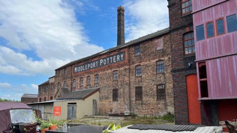 A 19th-century brick factory with a chimney coming out of the top and "Middleport Pottery" at the top of the wall in white letters. 