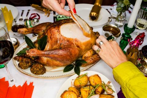 two hands take a slice of turkey from a roast turkey