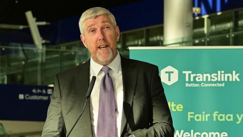 John O'Dowd stands in the new grand central station when it opened in early September. He has grey hair and wears a grey suit with a lilac tie.