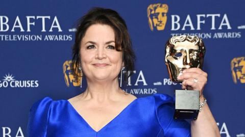 Ruth Jones wearing a blue dress holding her Bafta award and smiling