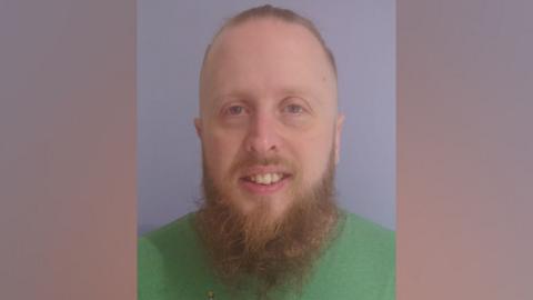 A man with red hair and beard, wearing a green t-shirt 