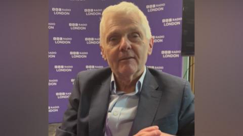 Tony Travers sitting in front of BBC Radio London branding