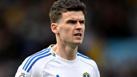 Sam Byram wearing a Leeds shirt looks to his right with a slightly open mouth
