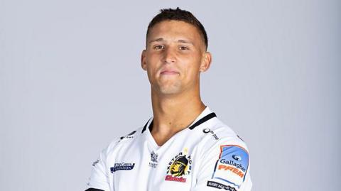 Harry Ascherl wearing Exeter kit standing with his arms folded looking at the camera
