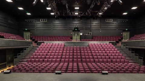 An empty theatre stadium with red chairs lined and bright lights on the stage 