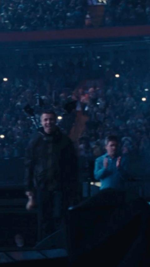 Liam and Noel walking on stage, it is dark and there are phone torches lit in the packed crowd