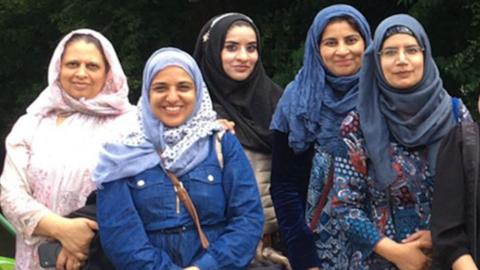 Five of the women in the group, standing and smiling, all wearing hijabs 