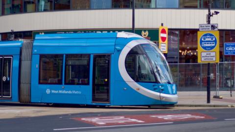 A blue tram with West Midlands Metro on the side on a Wolverhampton street, with bus lane signs.
