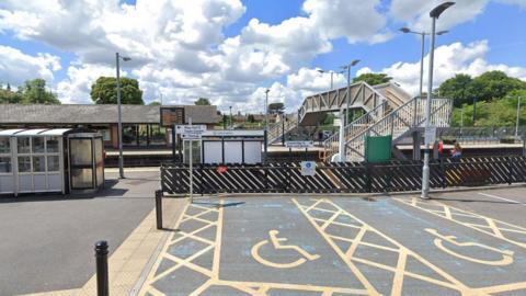 Two disabled parking bays next to Trowbridge train station on a sunny day. Two people are waiting on the platform.