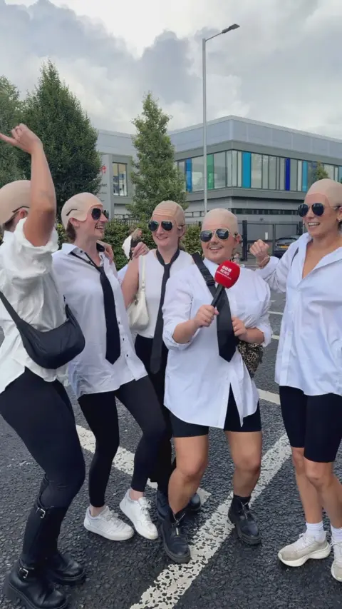 Group of people in bald caps and white shirts. 