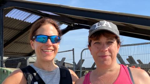 Two visitors to the harbour area look at camera one wearing sunglasses and the other is wearing a grey hat