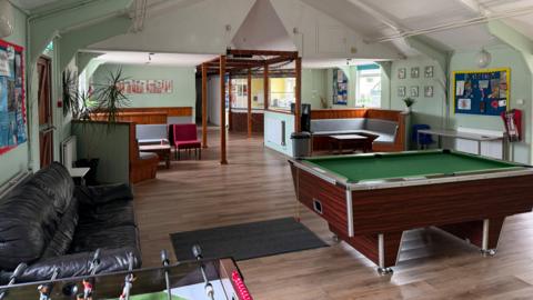 The inside of Chard youth centre with a pool table and table football on a wooden polished floor with seating around the edge of the room