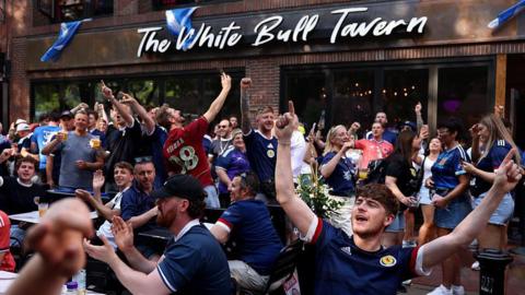 A group of Scotland fans cheer outside a bar called The White Bull Tavern.