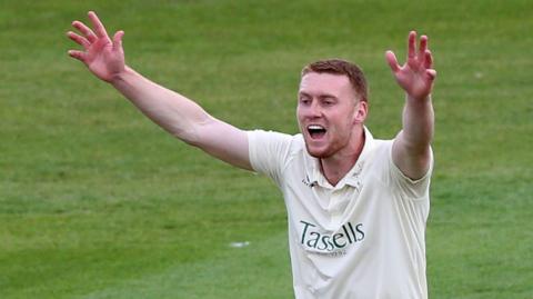 Joey Evison appeals with arms aloft, wearing Kent's all-white cricket kit