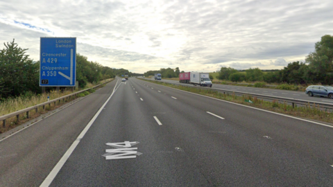 A Google street view showing the approach to junction 17 of the M4 motorway. It is a three lane road with a slip road coming up on the left. There is a blue motorway sign telling drivers that London and Swindon are straight ahead and that the junction leads Chippenham and Cirencester 
