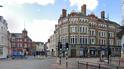 Buildings are on either side of several roads that cross in the city centre by a set of traffic lights.