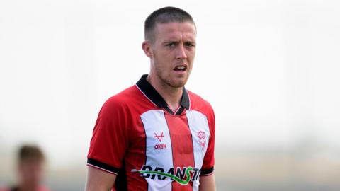 Jack Moylan looks at the camera as he plays in a preseason friendly for Lincoln City in their red and white striped home kit in July